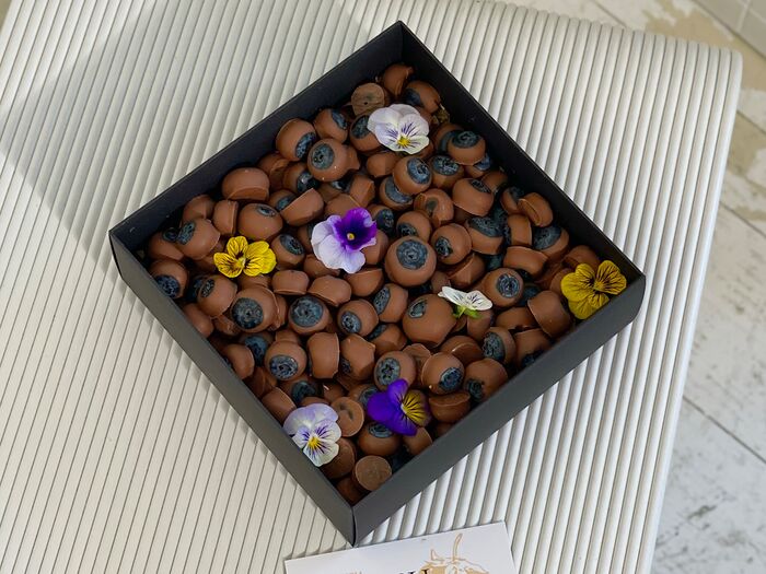 Голубика в молочном шоколаде 550 грамм, добавлены съедобные цветы Виола в количестве 7 штук, упакованы в черную коробочку